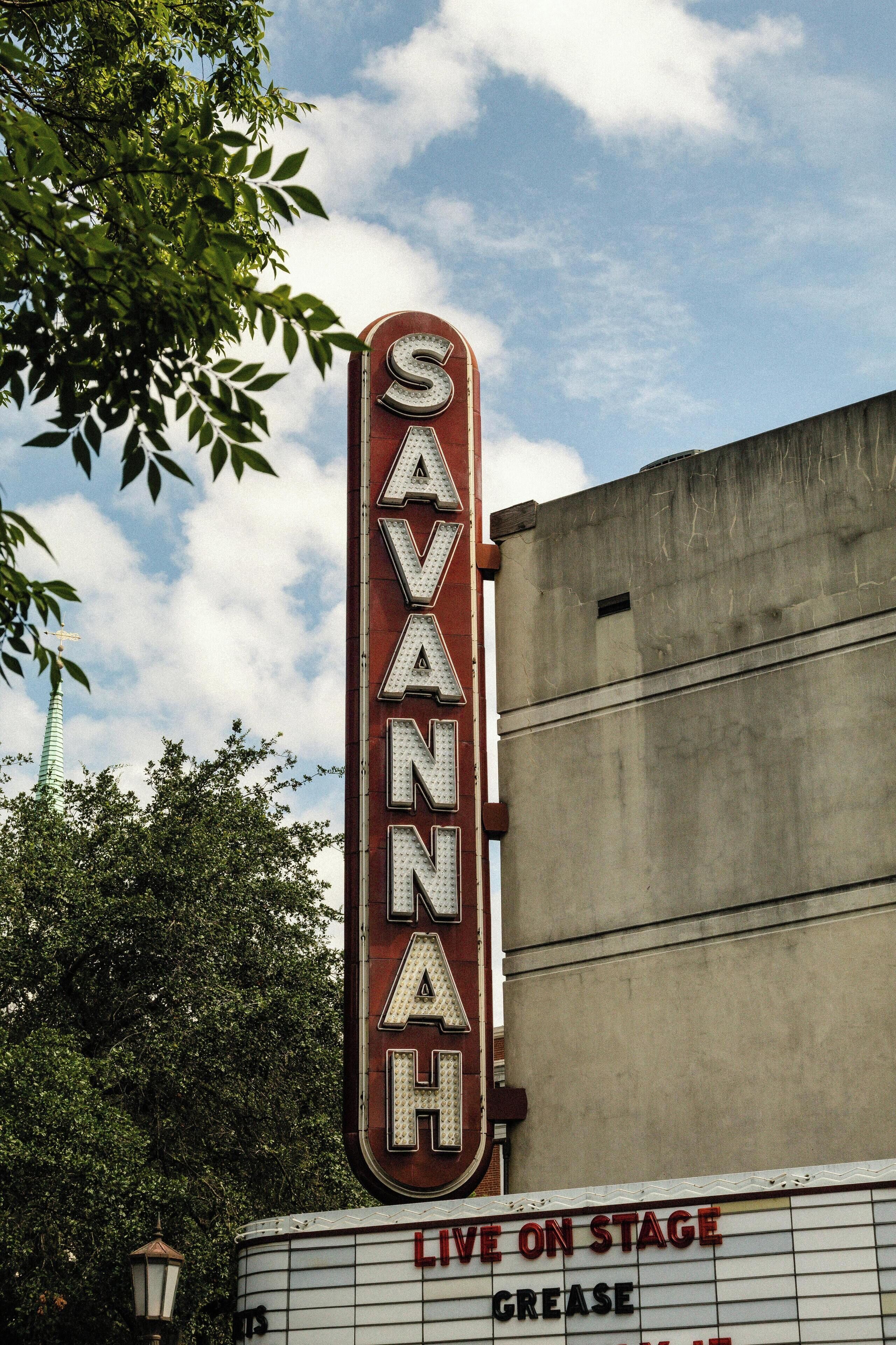 A vintage theater marquee with the name "SAVANNAH" and a sign below stating "LIVE ON STAGE GREASE".