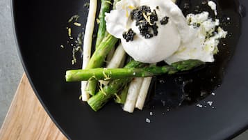 A black plate with roasted asparagus and a dollop of cream on a wooden board.