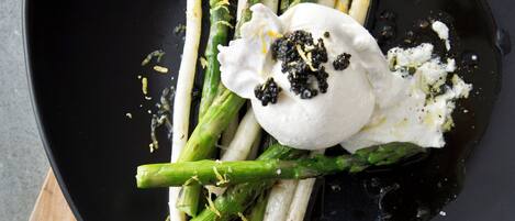 A black plate with roasted asparagus and a dollop of cream on a wooden board.