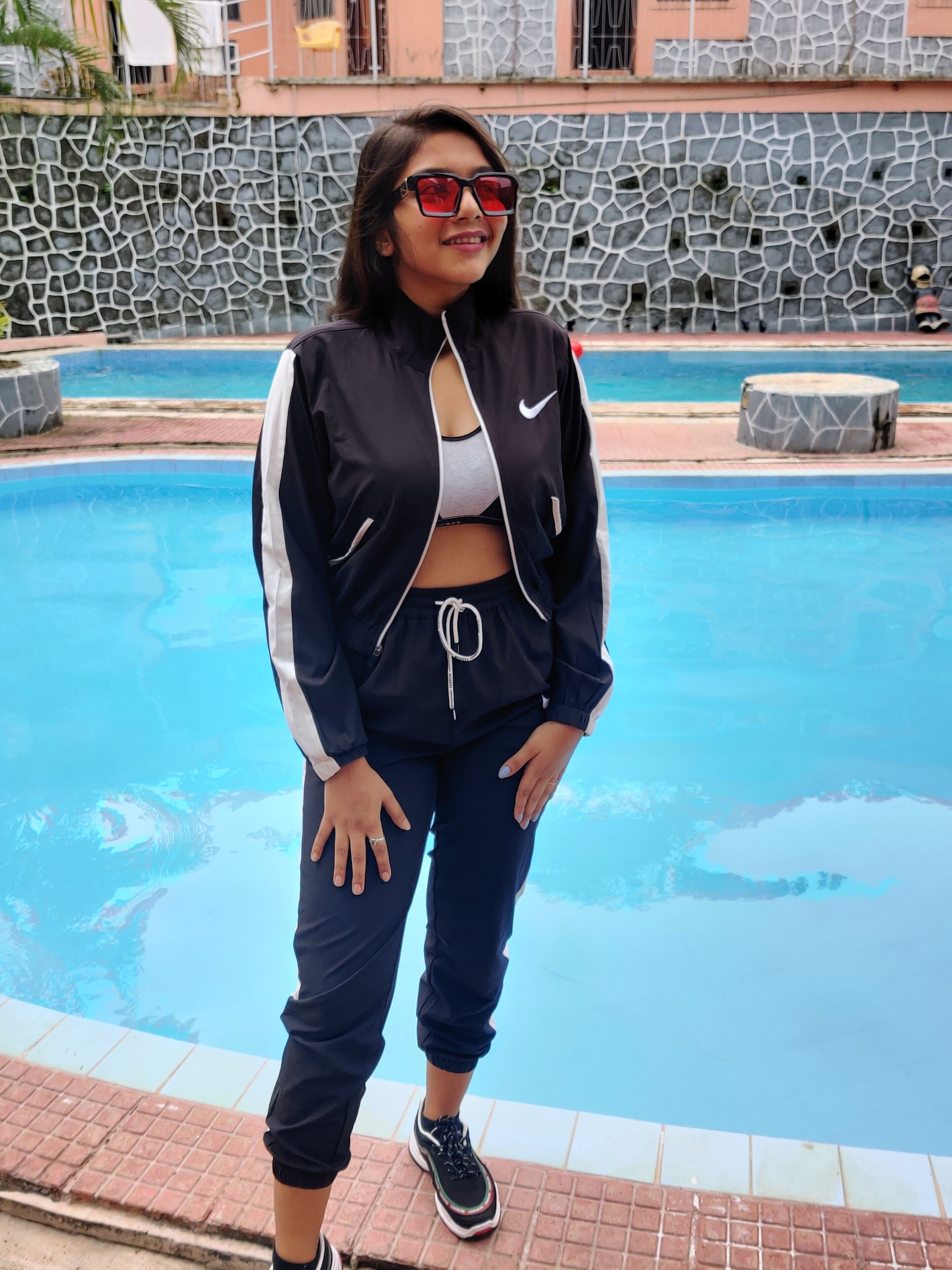A person standing by a swimming pool with a stone wall and a building in the background.