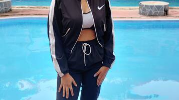 A person standing by a swimming pool with a stone wall and a building in the background.