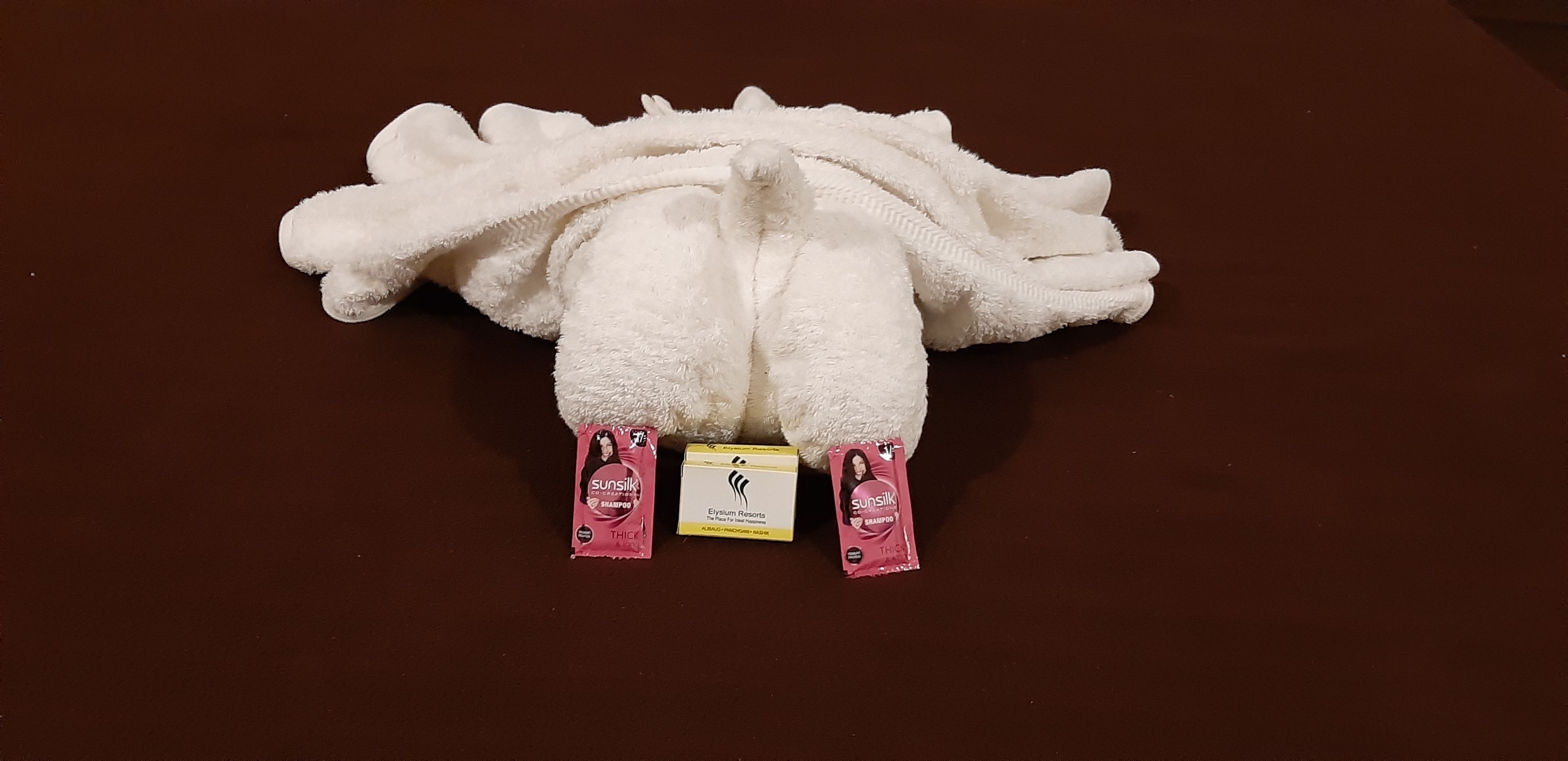 A plush white towel with two pink shampoo sachets and a small yellow tag.