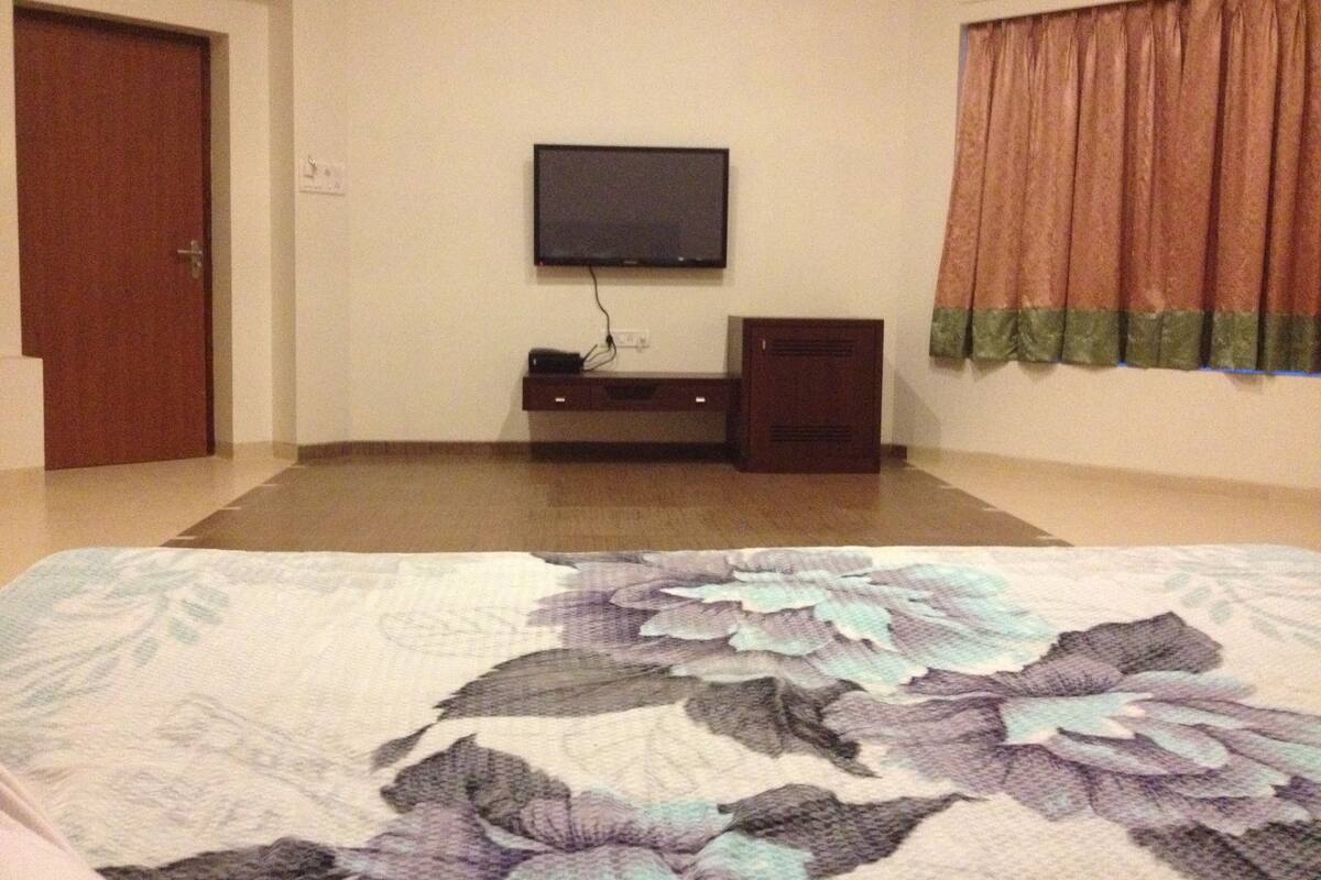 A room with a bed, a television mounted on the wall, a small cabinet, and a door.