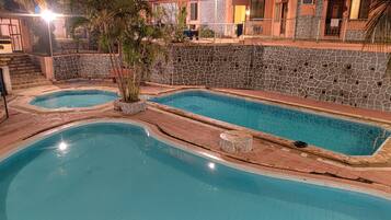 A swimming pool area with two pools, stone walls, and a building with a tiled roof in the background.