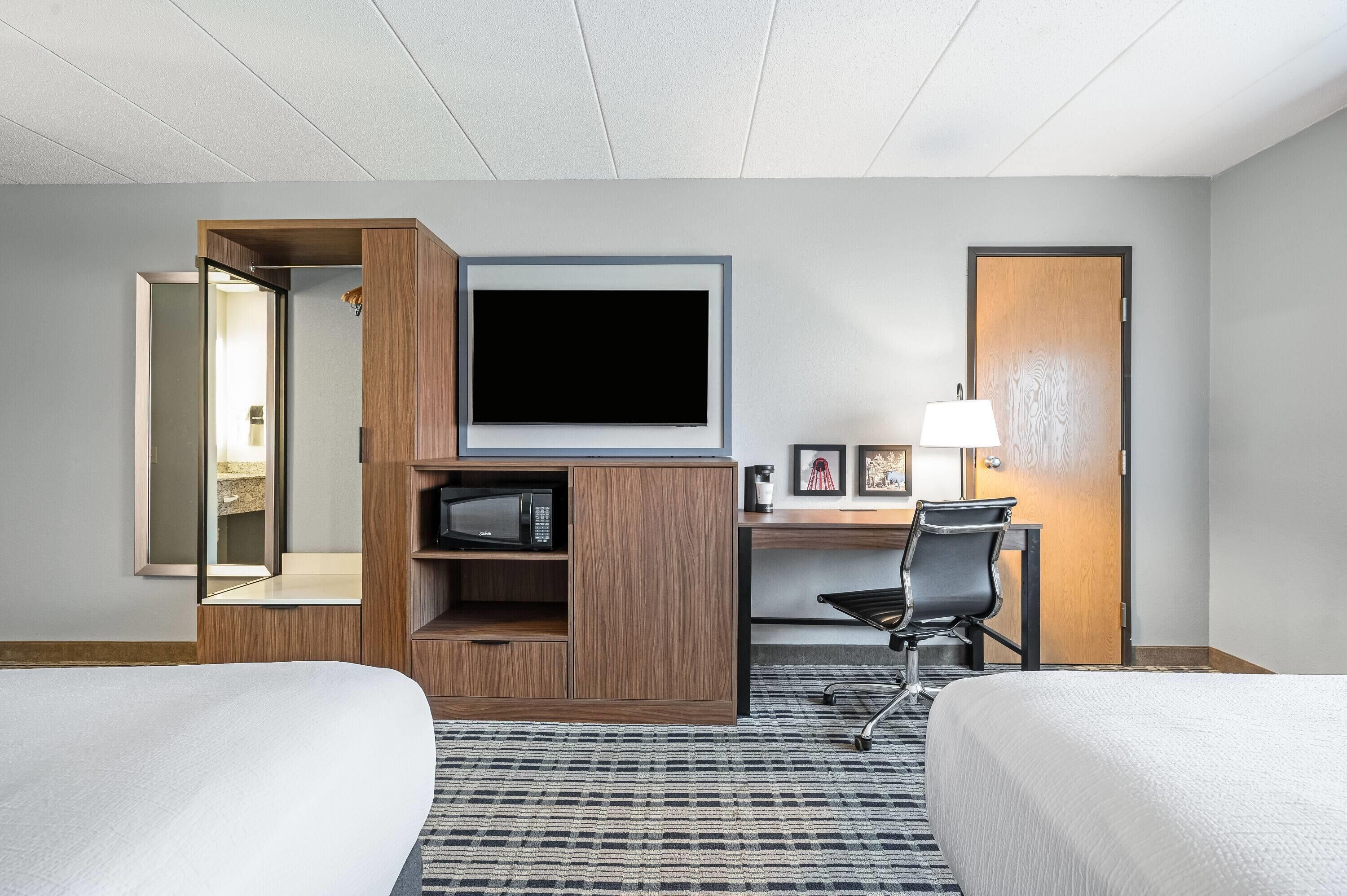 A hotel room with a bed, a desk with a chair, a television, and a lamp.