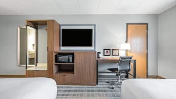 A hotel room with a bed, a desk with a chair, a television, and a lamp.