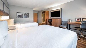 Ett hotellrum med två sängar, ett skrivbord, en stol, en TV och en garderob.