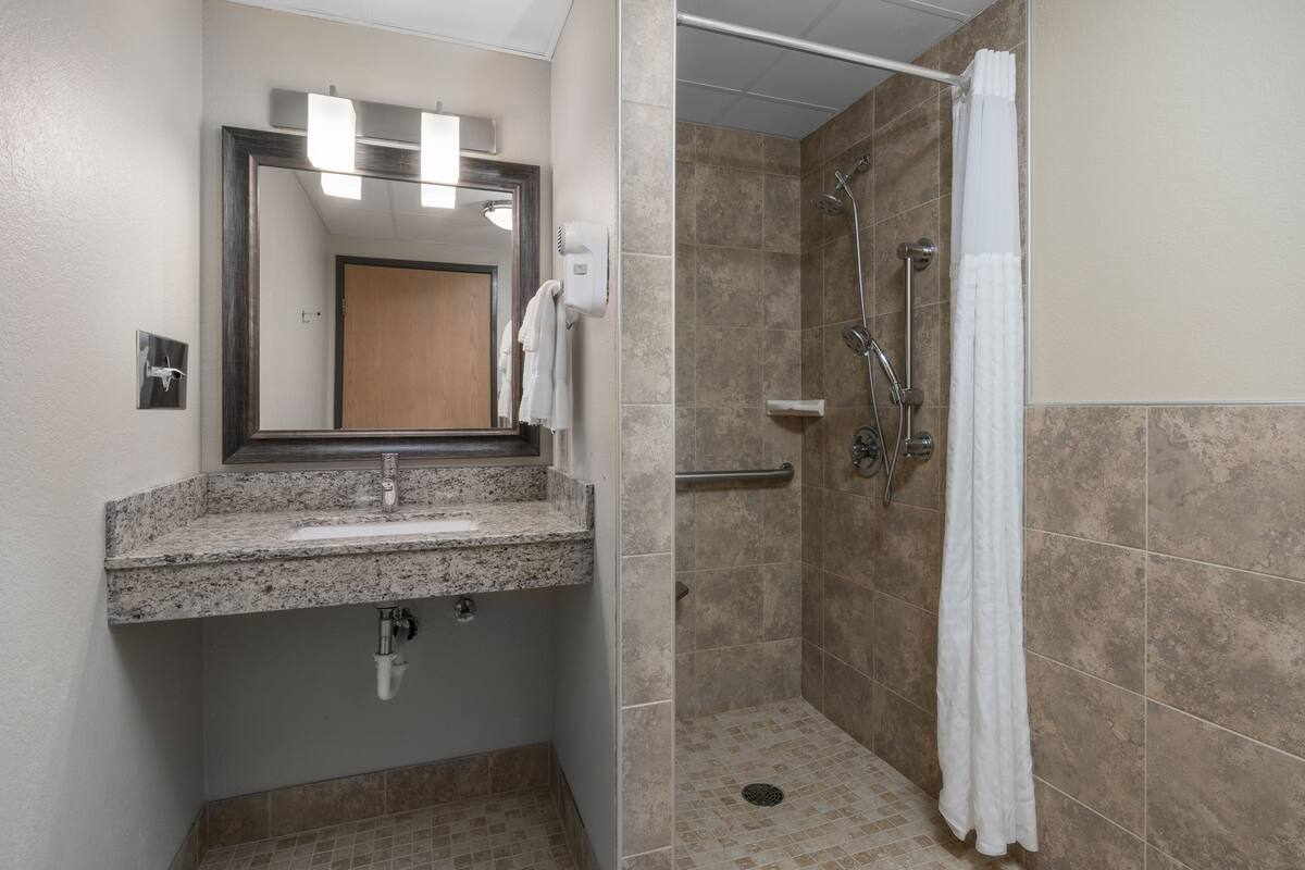 A bathroom with a granite countertop sink, a mirror, a towel rack, a shower with a glass door, and beige tiled walls.