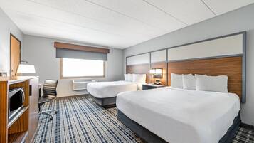A hotel room with two beds, a desk, a chair, a lamp, a heater, and a patterned rug.