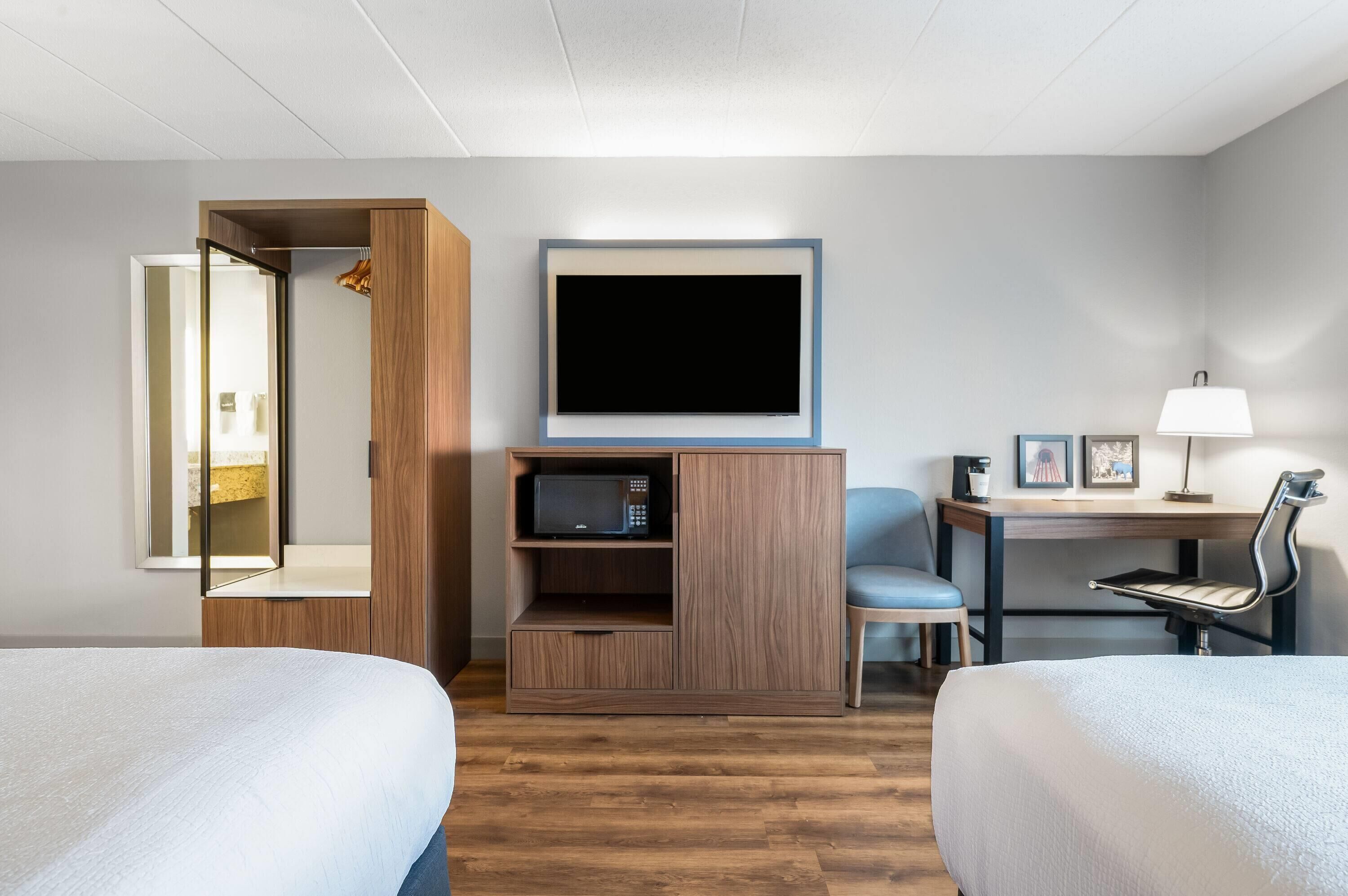 Habitación de hotel con dos camas, televisor, escritorio con silla y armario.
