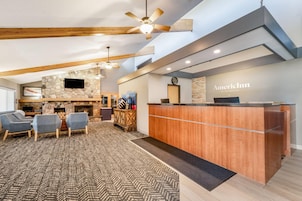 Un hall de hotel con mostrador de recepción, zona de estar, chimenea y pared de piedra.