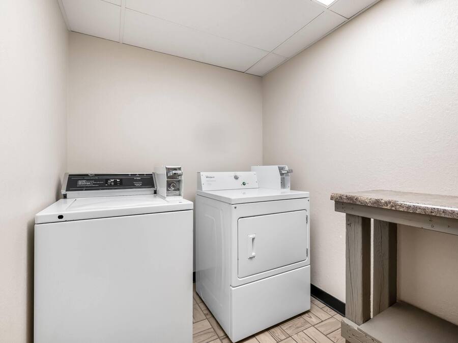 A laundry room with a front-loading washer and dryer, a wooden bench, and a tiled floor.