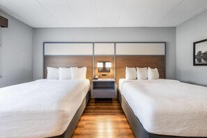 A hotel room with two beds, a wooden headboard, a nightstand with a lamp, and a framed picture on the wall. - AmericInn by Wyndham Bemidji (Bemidji)