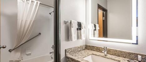 A bathroom with a shower, toilet, sink, and a large mirror.
