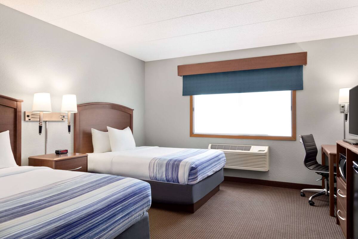 Ein Hotelzimmer mit zwei Betten, einem Schreibtisch, einem Sessel, einem Fernseher und einem Fenster mit Blick.