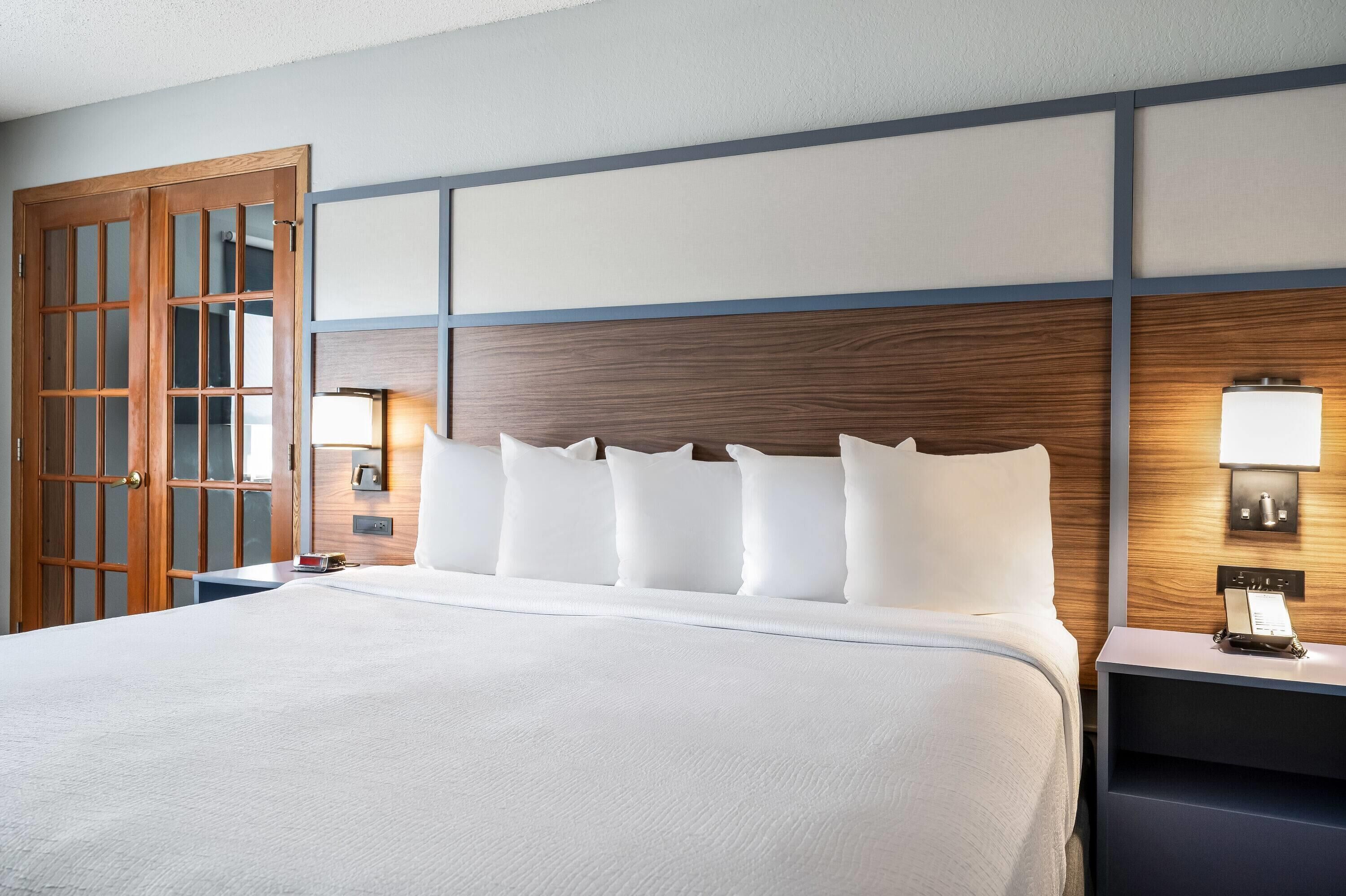 Habitación de hotel con una cama grande, cabecera de madera, lámparas de noche y una puerta de madera.