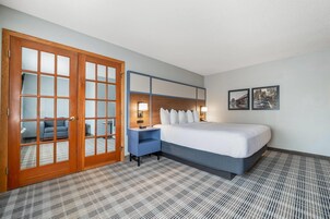 Habitación de hotel con cama, escritorio, silla, armario y dos cuadros en la pared.
