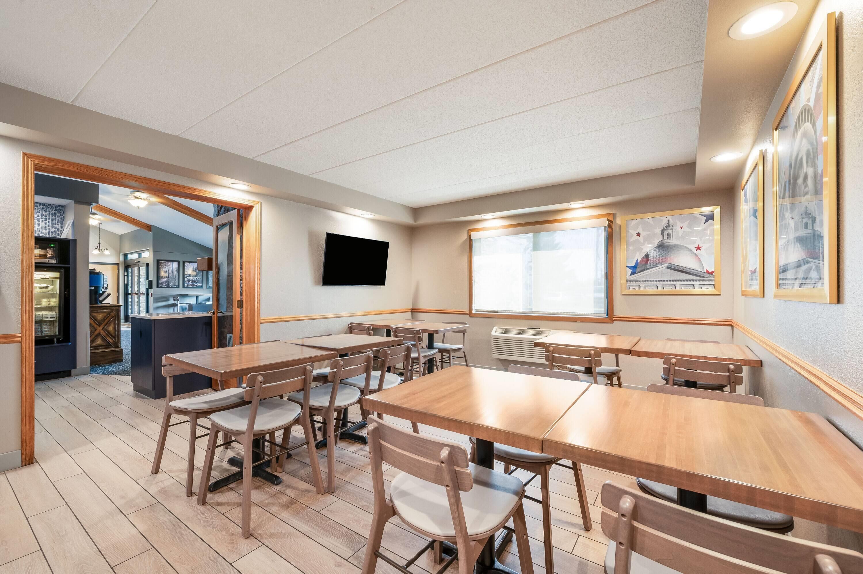 Un restaurant avec des tables et des chaises en bois, un téléviseur à écran plat fixé au mur et des œuvres d’art encadrées qui décorent les murs.