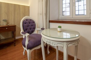 Una habitación con una butaca tapizada de púrpura, una mesa blanca ornamentada y un armario de madera.