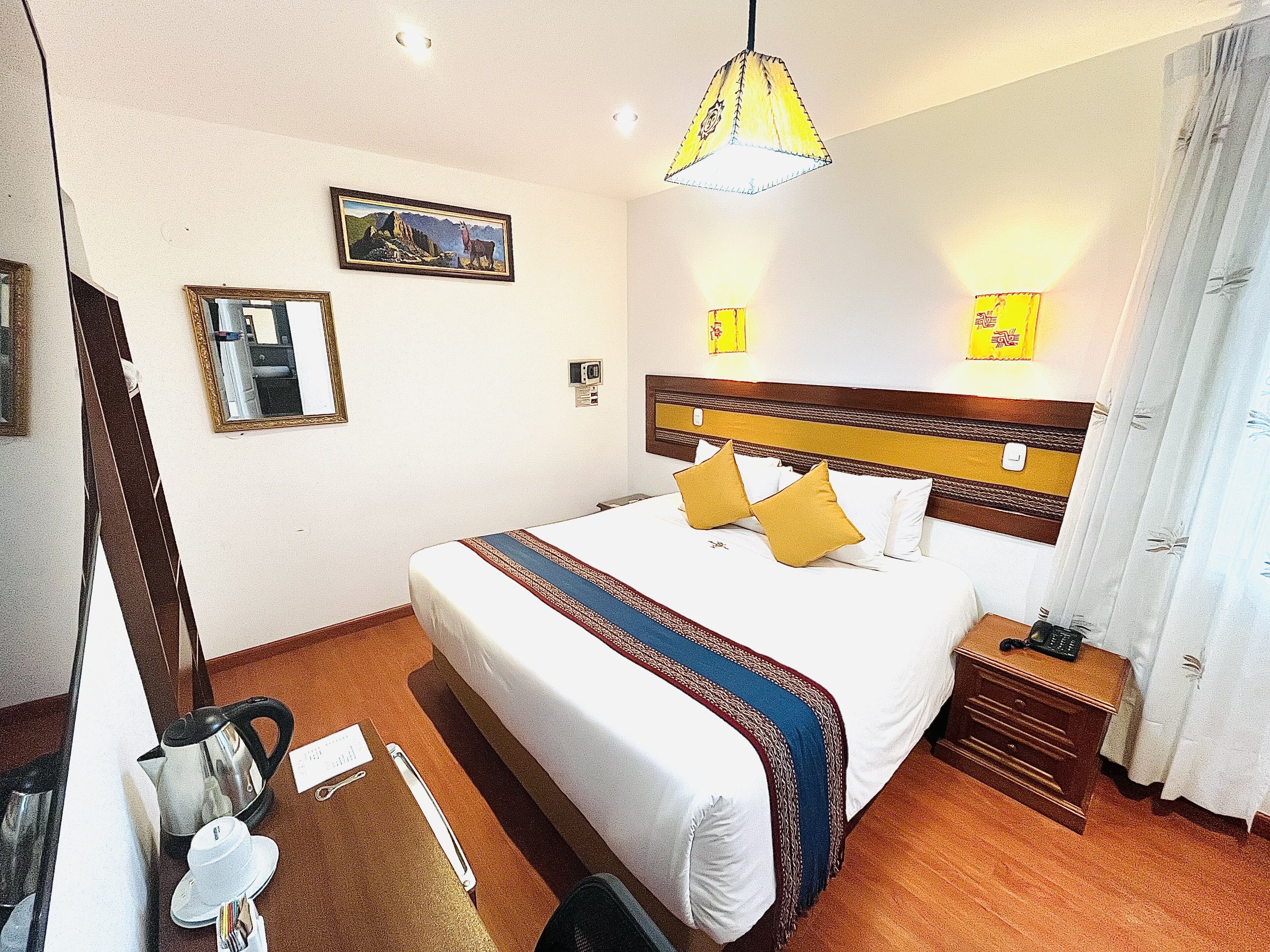 Habitación de hotel con una cama grande, mesitas de noche, un espejo, un cuadro en la pared y una lámpara de techo.