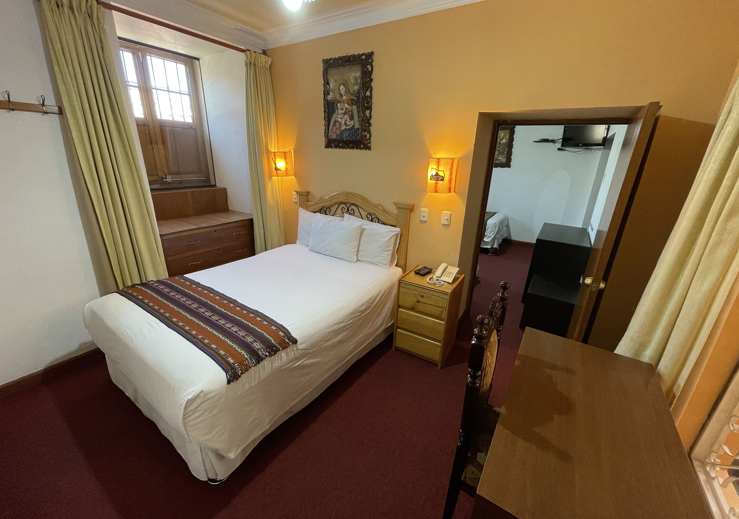 A hotel room with a bed, bedside table, lamp, and a window with curtains.