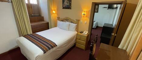 A hotel room with a bed, bedside table, lamp, and a window with curtains.