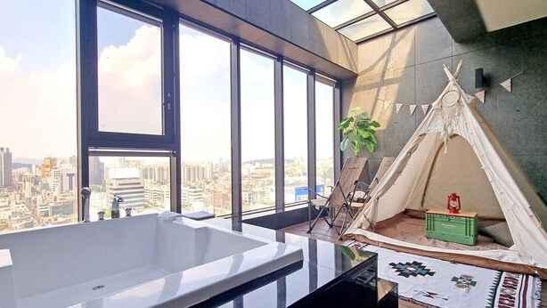 A modern bathroom with a large bathtub, a city view through large windows, and a small teepee-like structure with a lantern. - SR Hotel Sadang (Seoul)
