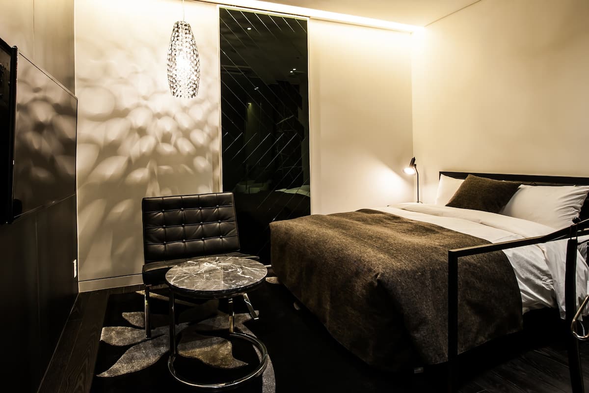 A modern hotel room with a bed, a chair, a small table, and a large window.