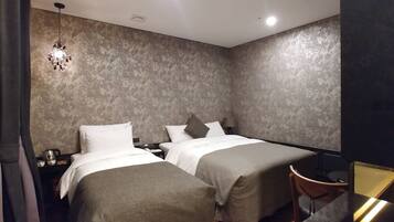 A hotel room with two beds, a nightstand, a lamp, and a chair.