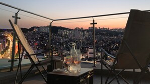 A balcony with a table set for two, featuring two glasses with "Happy Birthday" and a bottle. The balcony overlooks a cityscape at dusk. - SR Hotel Sadang (Seoul)