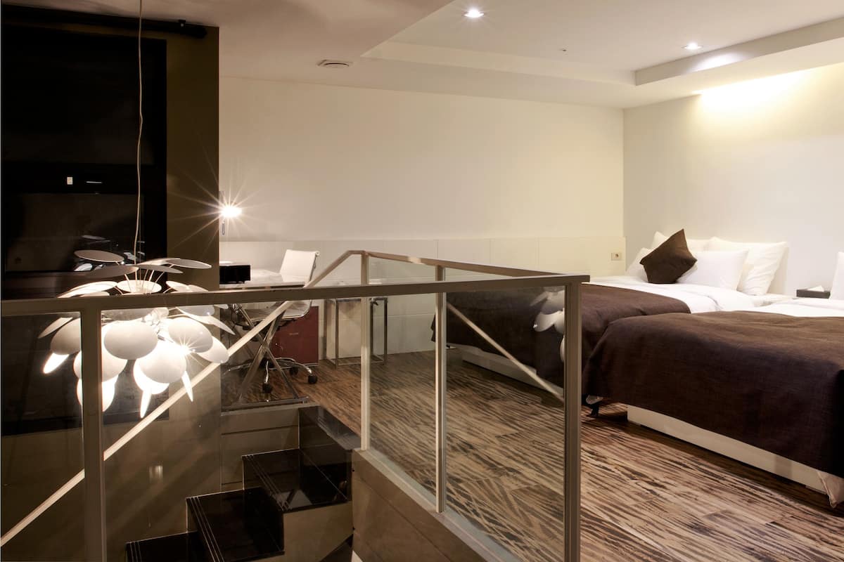 A modern hotel room with a glass staircase, a bed with a brown bedspread, and a flat-screen TV.