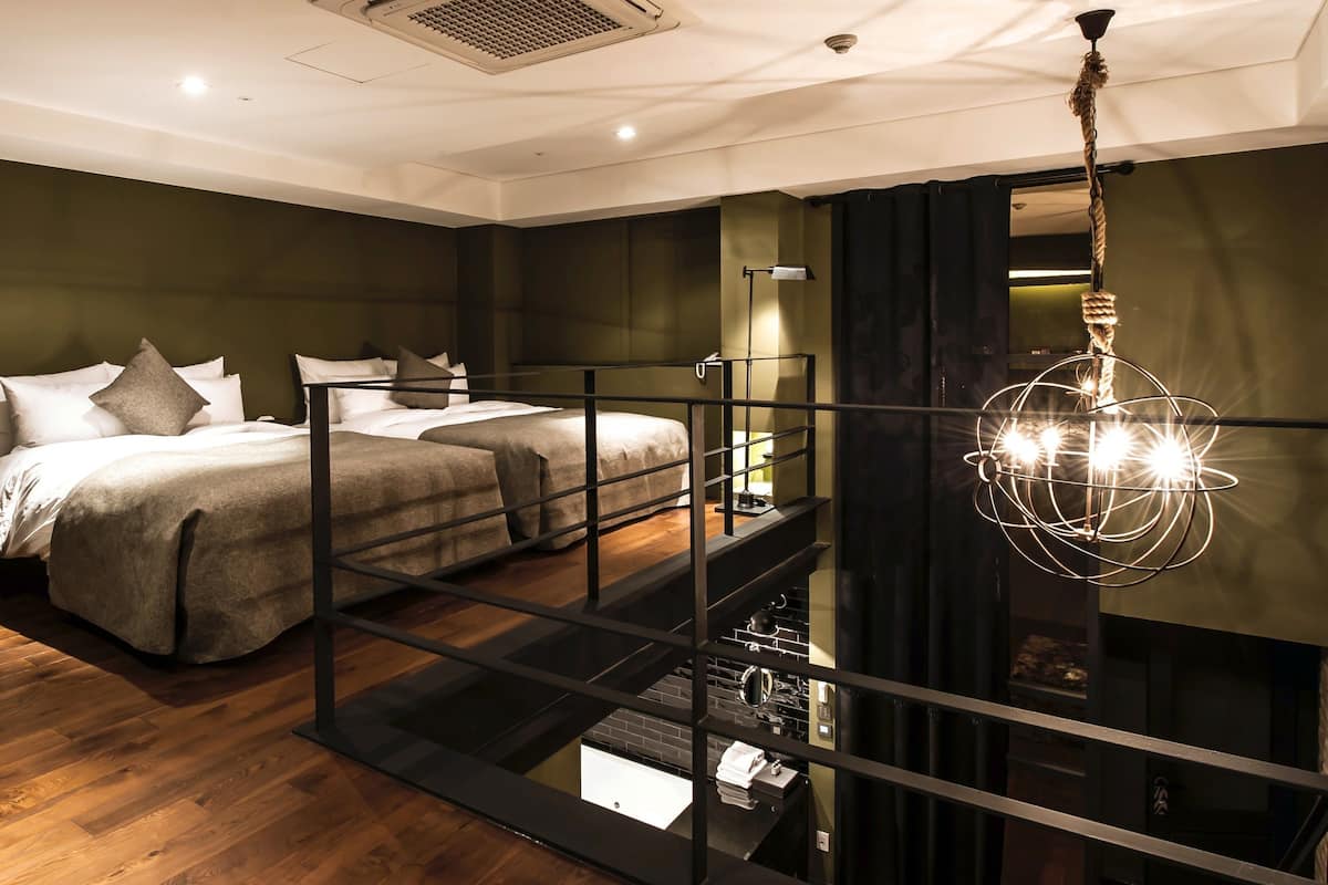A modern bedroom with a bed, a small table, a hanging light fixture, and a view of the outside through a window.
