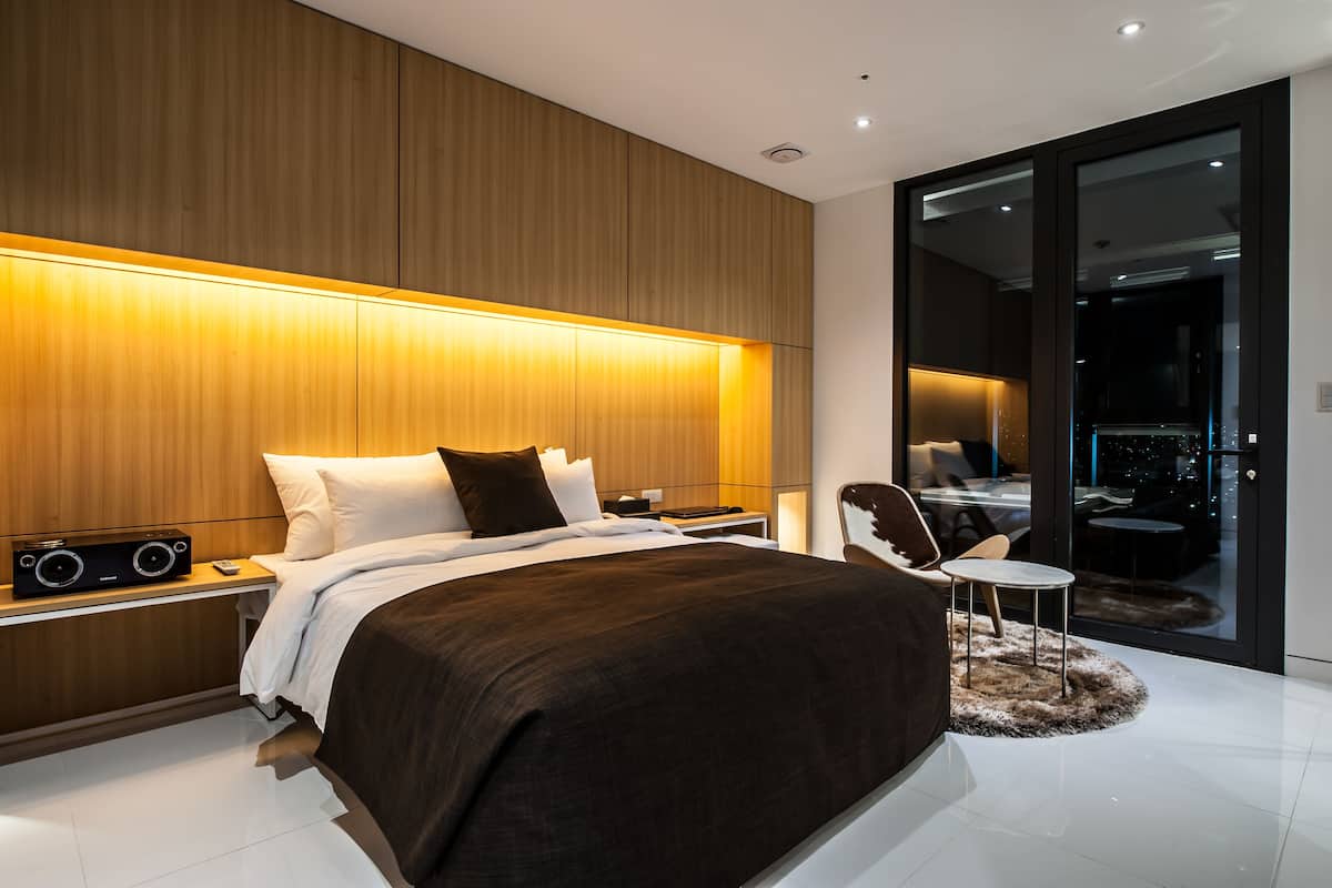 A modern bedroom with a large bed, bedside tables, a chair, and a view of the city through a glass door.