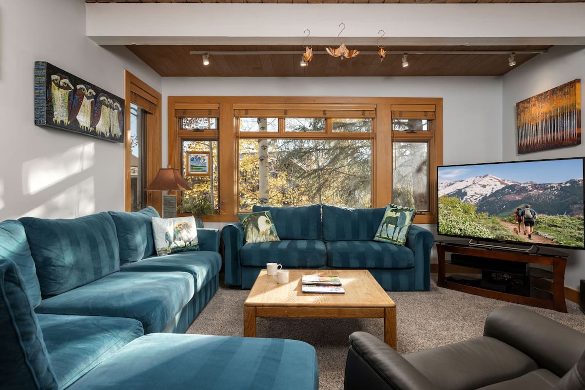 A living room with two blue sofas, a wooden coffee table, and a television displaying a mountain scene.