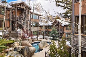 A resort with a pool surrounded by rocks and trees, wooden buildings with balconies, and a snowy landscape. - Aspenwood - CoralTree Residence Collection (Snowmass Village)