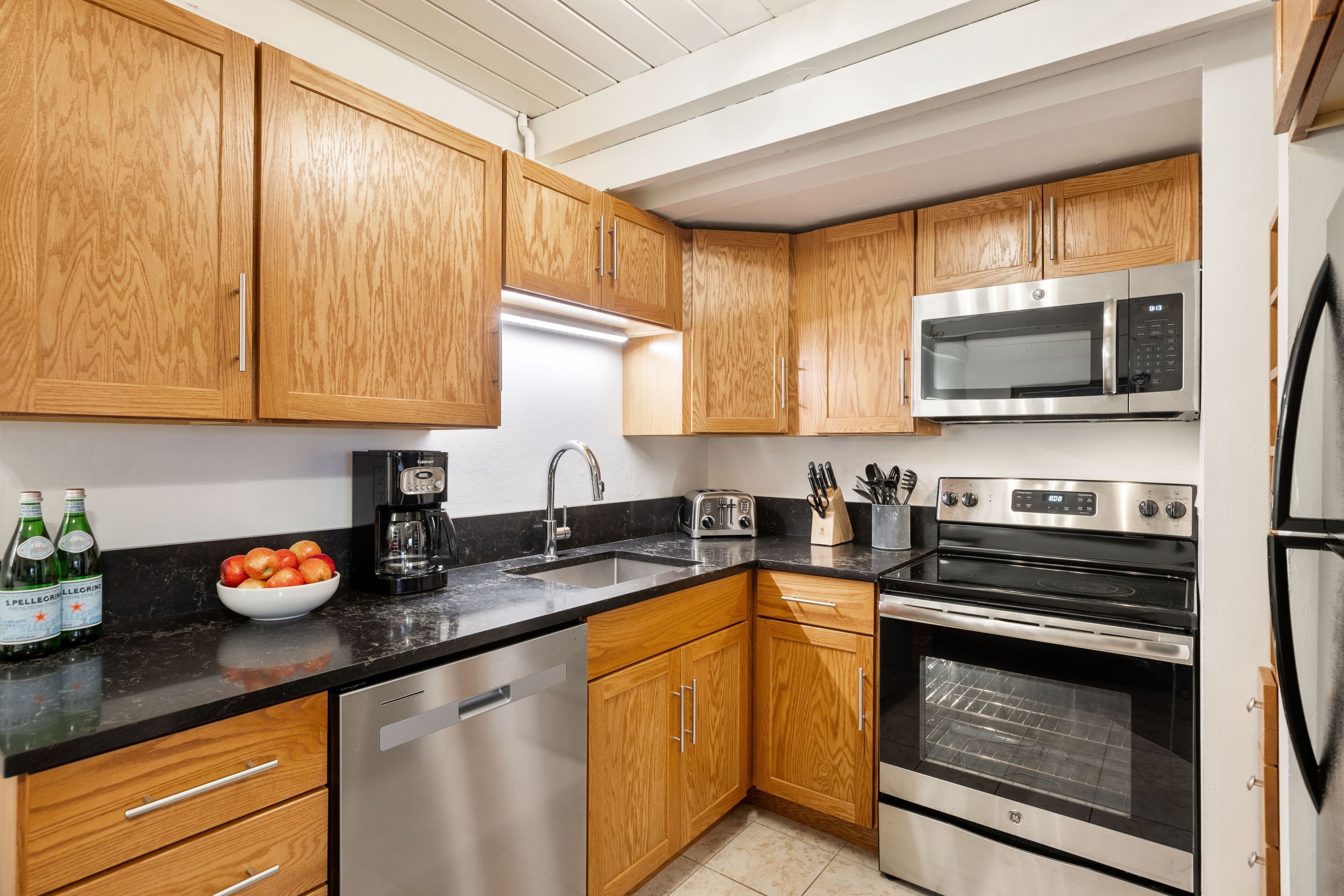 A modern kitchen with wooden cabinets, stainless steel appliances, and a black countertop.