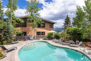 A pool area with lounge chairs, a stone wall, and a building with large windows. - Aspenwood - CoralTree Residence Collection (Snowmass Village)