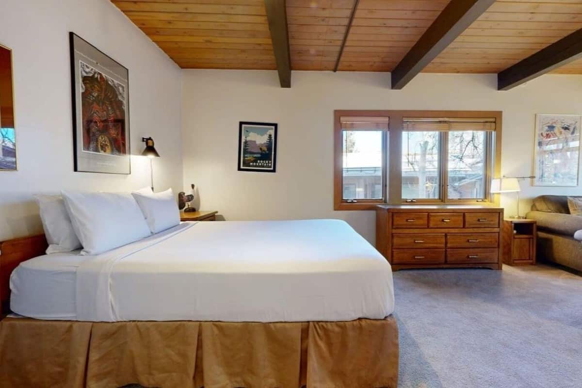 A bedroom with a large bed, a dresser, a nightstand, and a window with a view of trees.