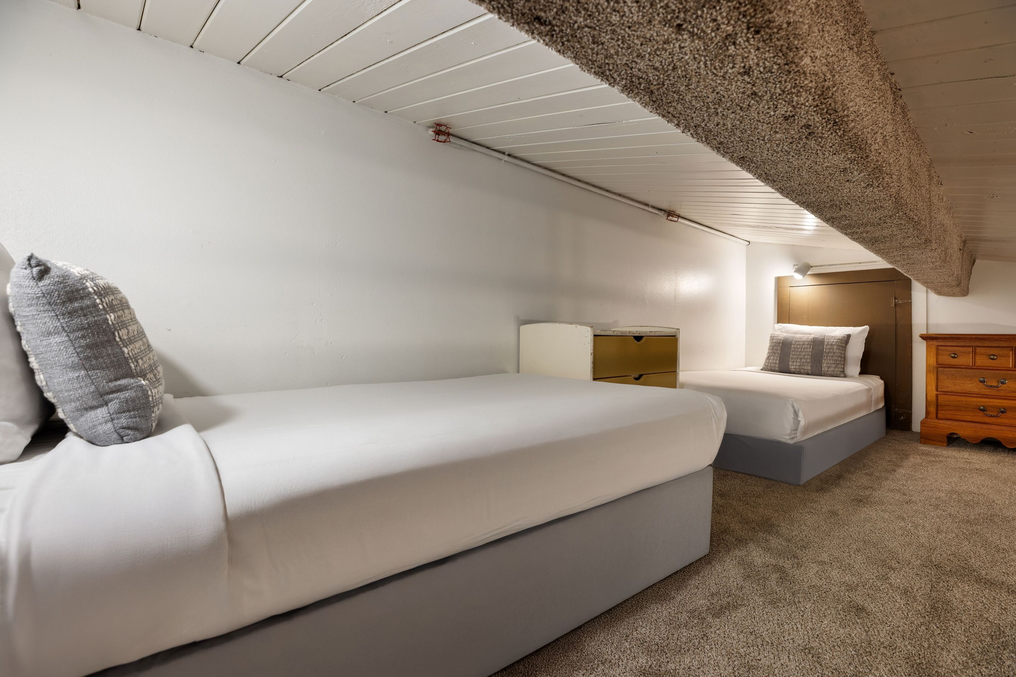 Een slaapkamer met twee bedden, een houten dressoir en een plafond met zichtbare balken.