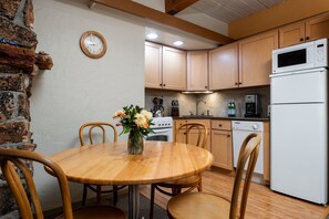 A kitchen with wooden cabinets, a white refrigerator, a stove, and a dining table with chairs. - Aspenwood - CoralTree Residence Collection (Snowmass Village)