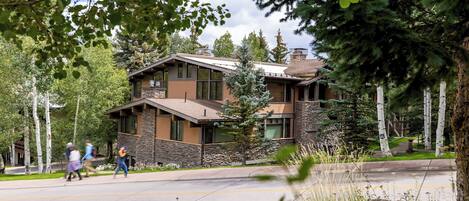 A modern two-story building with a stone facade and large windows, surrounded by trees and a clear sky.