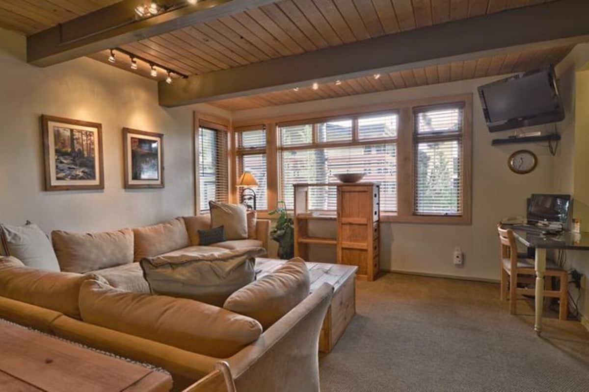 A cozy living room with a sectional sofa, a wooden coffee table, and a television mounted on the wall.