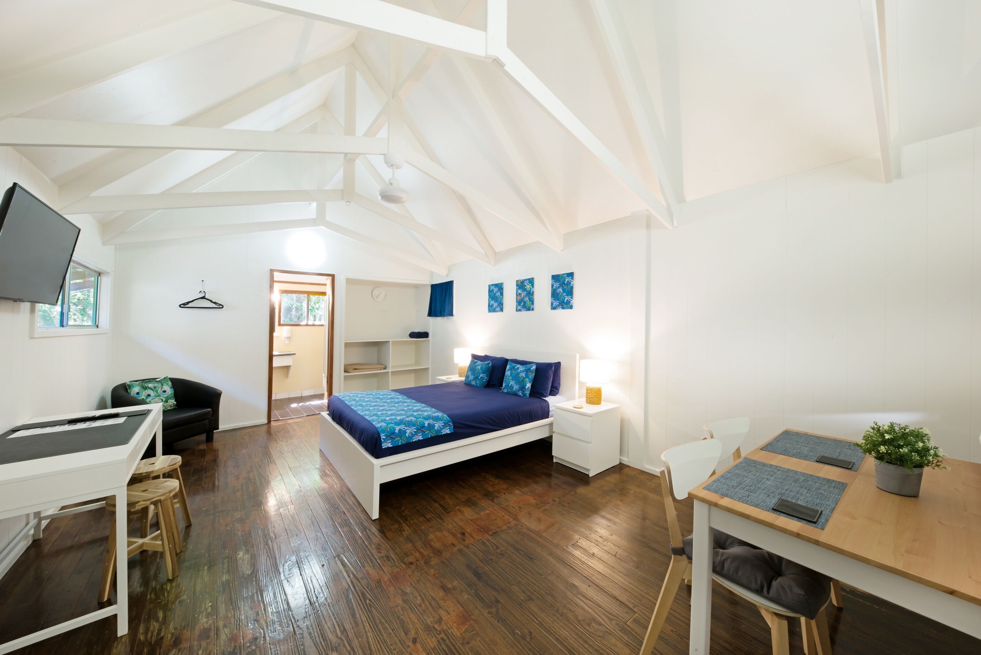 A bedroom with a bed, bedside tables, a desk, a chair, a TV, and a hanging light fixture.