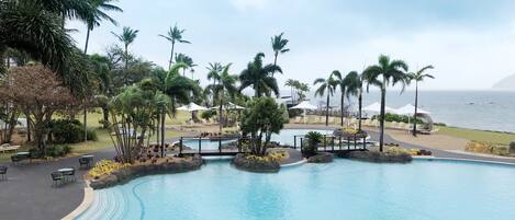 A swimming pool with a curved design, surrounded by palm trees and lounge chairs.