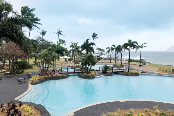 A swimming pool with a curved design, surrounded by palm trees and lounge chairs.