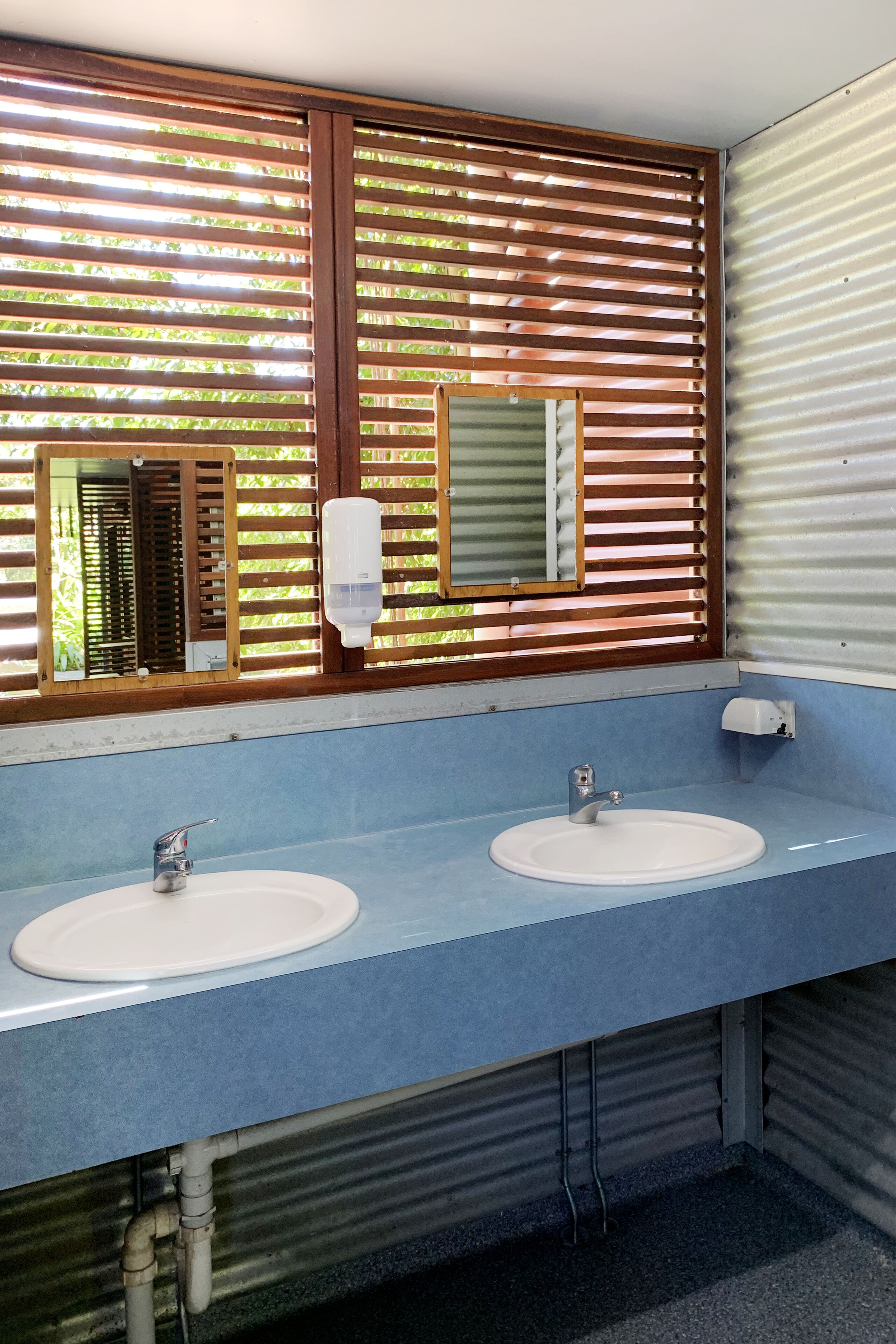 A bathroom with two sinks, wooden slatted windows, and a mirror.