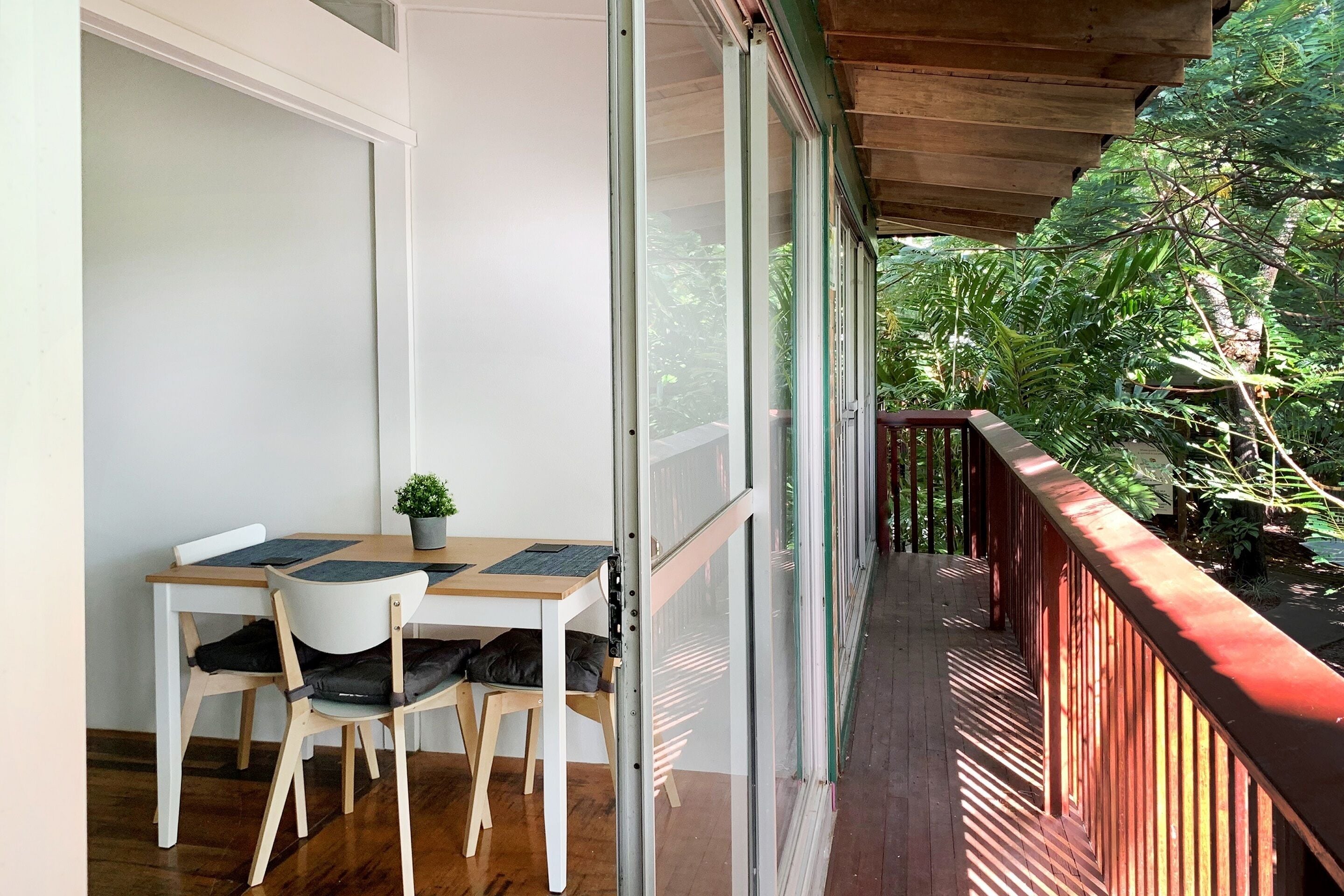 A balcony with a wooden railing, a table with chairs, and a potted plant.