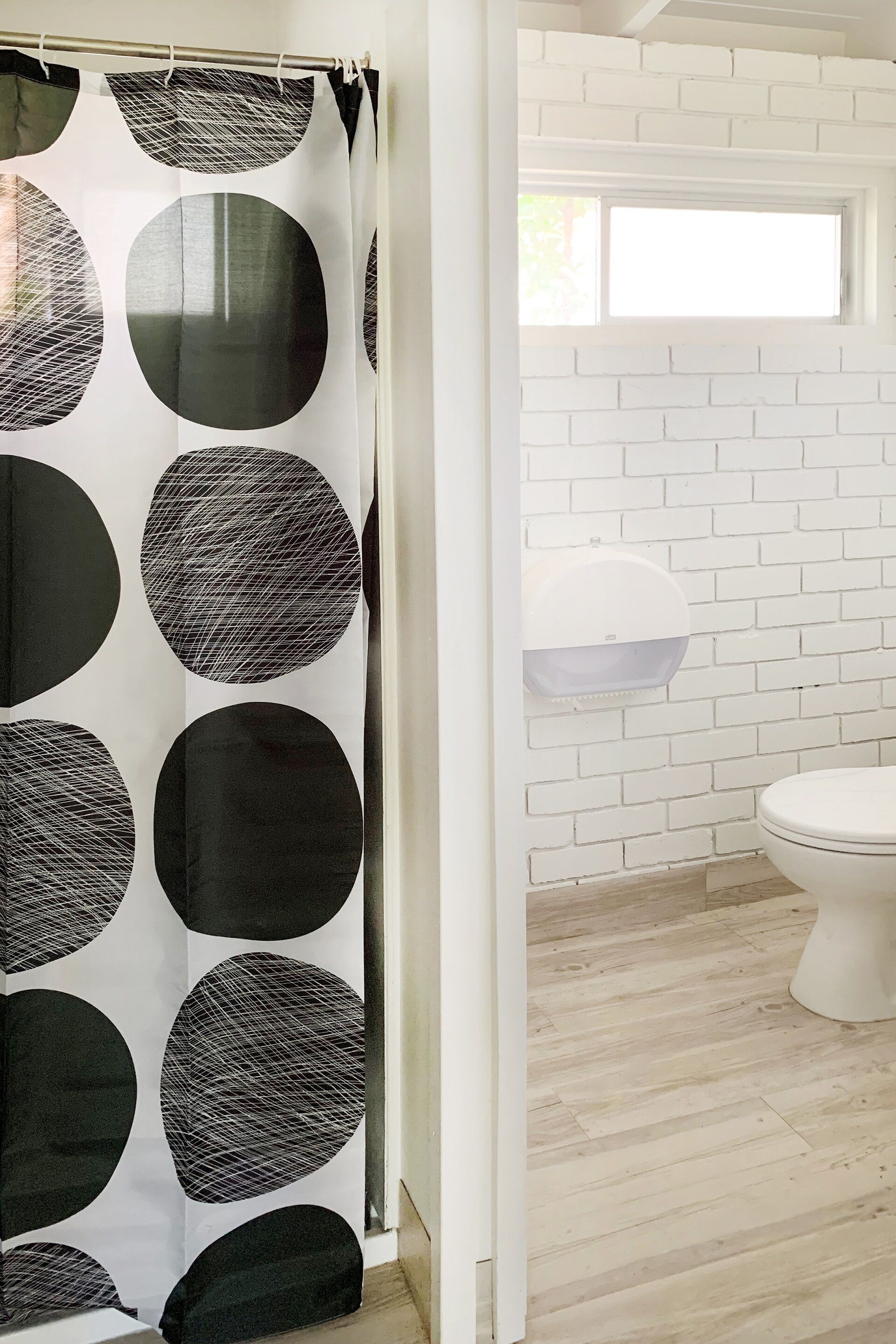 A bathroom with a white brick wall, a toilet, and a shower curtain with a geometric pattern.