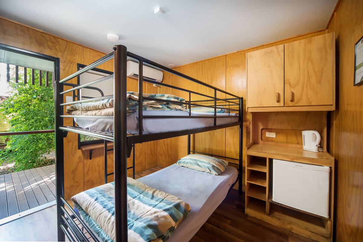 Een slaapkamer met een stapelbed, een klein kitchenette en een raam met uitzicht op groen.