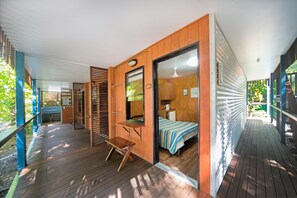 A compact, modern room with a wooden floor, a bed with a striped bedspread, a small table, and a bench.